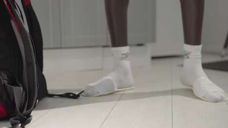 close-up view of person wearing white socks and slippers walking on light-coloured floor in indoor setting. comfortable home or apartment atmosphere with soft lighting