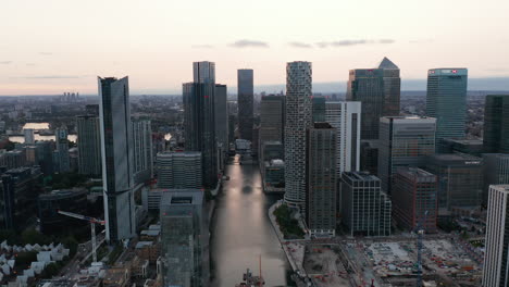 Tall-modern-office-buildings-along-water-channel-in-former-docks.-Iconic-skyscrapers-in-Canary-Wharf-after-sunset.-London,-UK