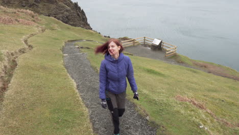 siga la foto de una niña feliz caminando al borde de los acantilados en escocia, isla de skye con el océano atlántico al fondo en un día nublado