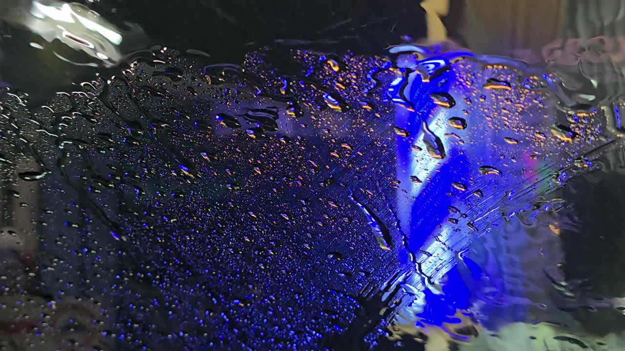 Nærbillede af regndråber på bilens forrude med blåt neonlys