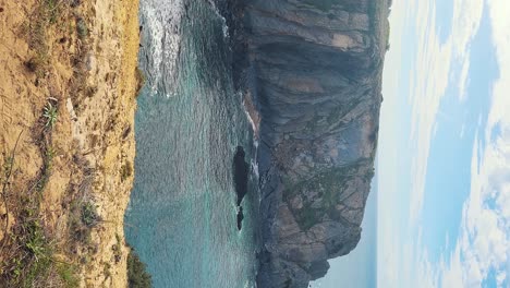 zambujeira do mar over the sea shore with ocean waves, cliffs and sand dunes covered by green vegetation red leaves of sour fig, sunny day, clear blue sky