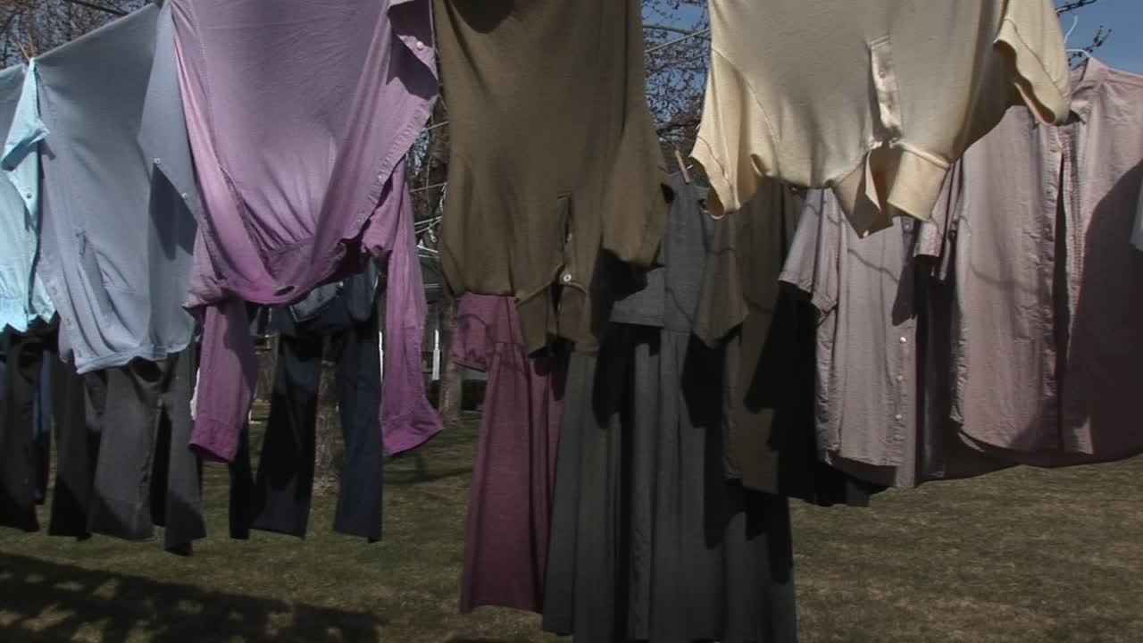 화려한 셔츠와 어두운 드레스는 큰 시골집 근처에서 말리기 위해 빨랫줄에 손을 얹는다