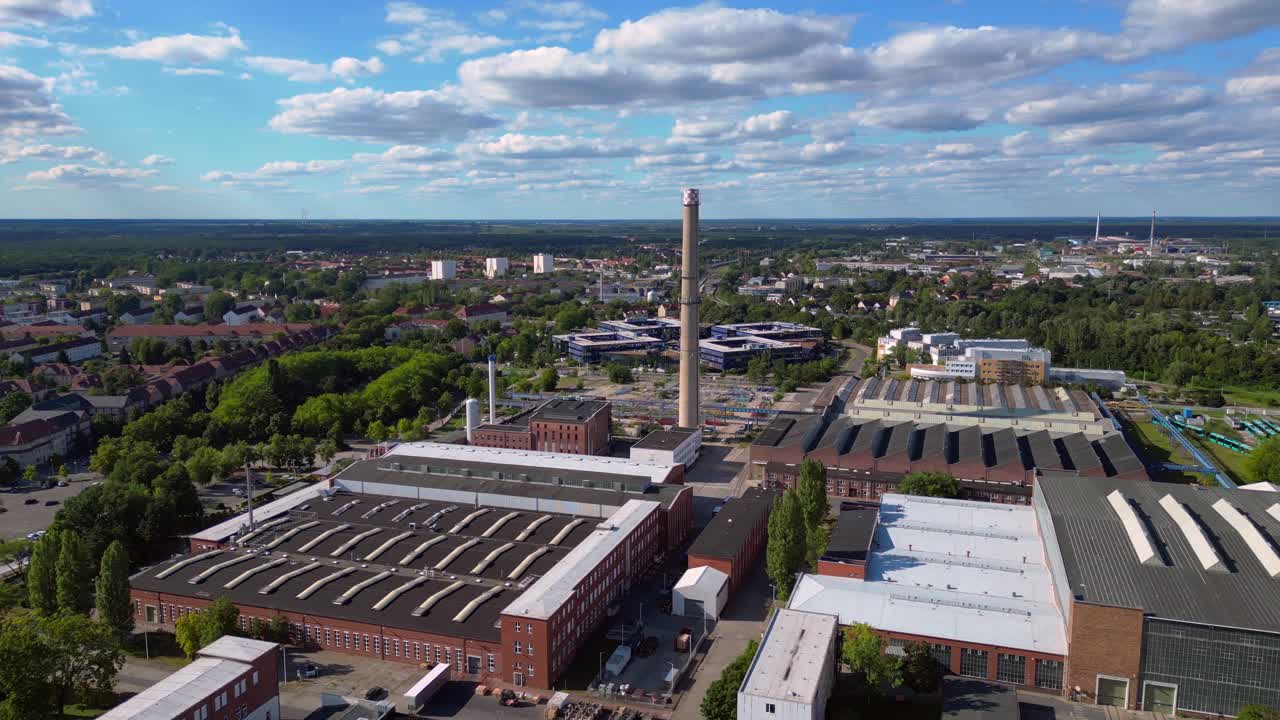 industrial buildings and a chimney in Hennigsdorf, Germany, with a train passing by. Amazing aerial view flight wide orbit overview drone