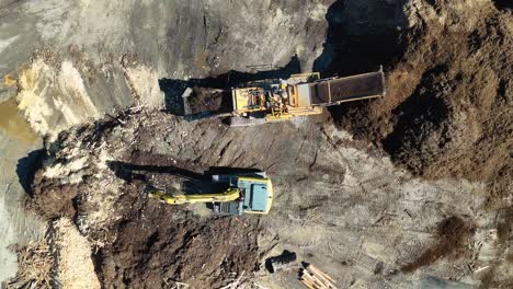 drone footage captures an excavator moving mulch in a dirt processing area under bright sunlight