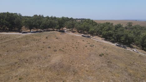 Soldados-Del-Escuadrón-De-Infantería-Del-Ejército-De-Israel-En-Un-Vehículo-Que-Conduce-A-Través-De-Un-Campo-Verde-En-La-Carretera-Rural-Del-Campo-De-Entrenamiento,-Tiro-De-Seguimiento-Aéreo