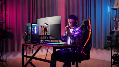 un adolescente asiático emocionado celebra la victoria y baila mientras juega videojuegos en la computadora.
