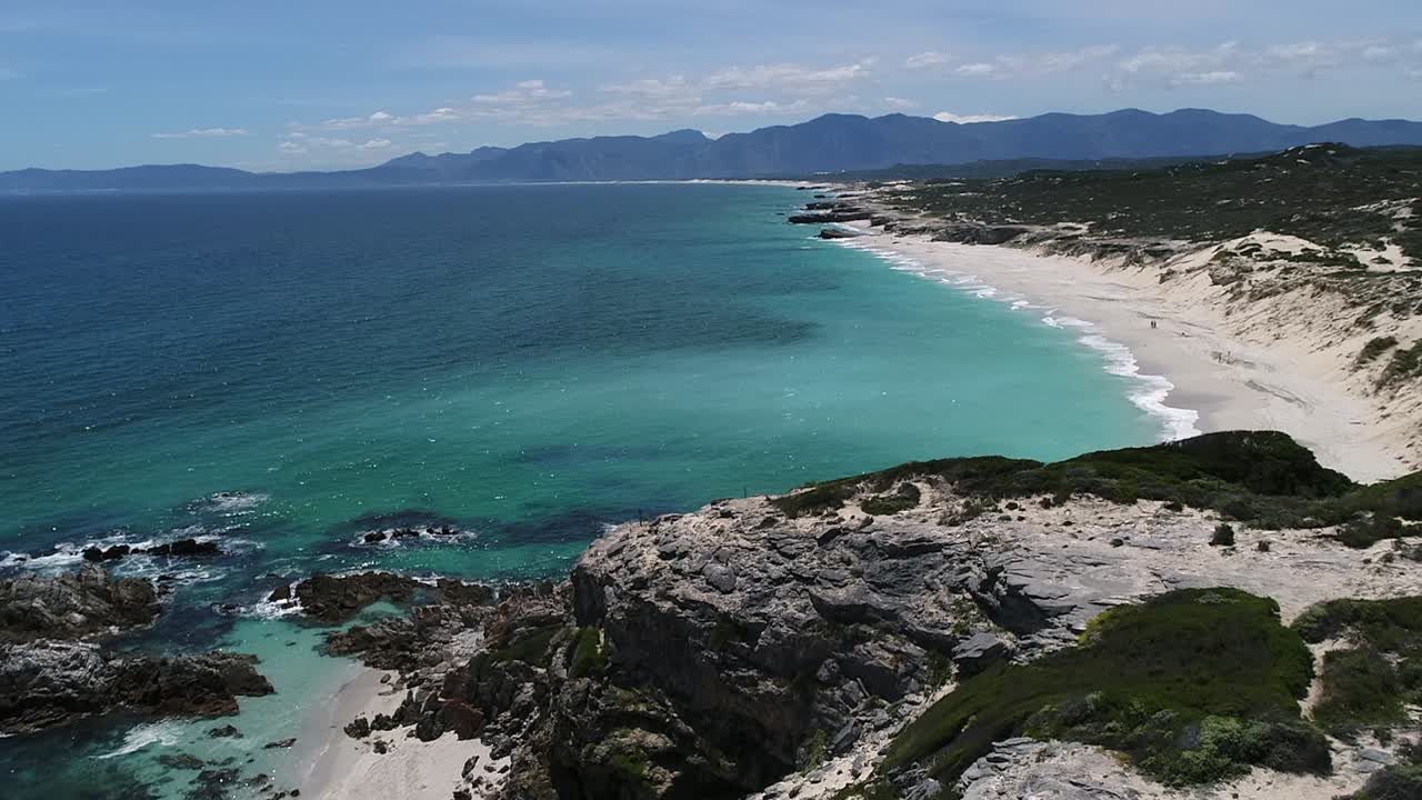 Sorvolo di un promontorio roccioso fino a una spiaggia di sabbia bianca su una costa oceanica arida