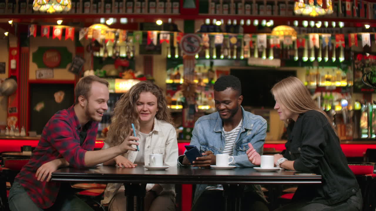Multinational company of friends in a restaurant looking at the phone by phone and discussing photos smiling and laughing..