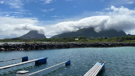hermosa toma panorámica de un pequeño puerto deportivo en un día soleado con montañas cubiertas de nubes en el fondo y el viento ondulando el agua