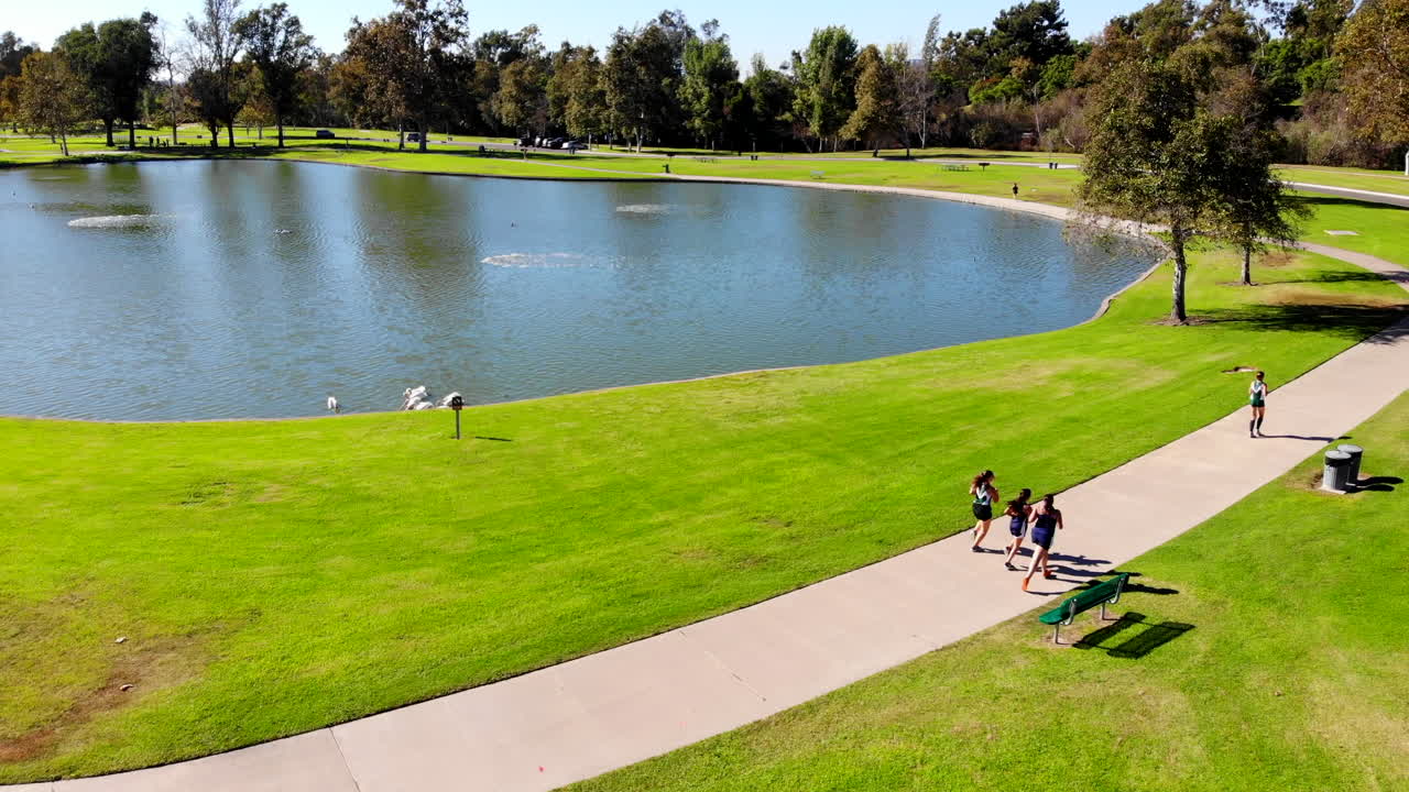 女子高中越野跑者在艾爾文的梅森區域公園的湖邊經過, ca 拍攝是空中 4k 無人機
