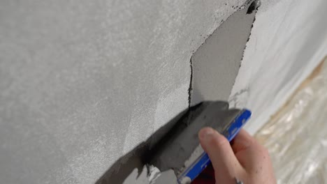 un hombre está aplicando yeso decorativo a una pared gris - primer plano en la pared