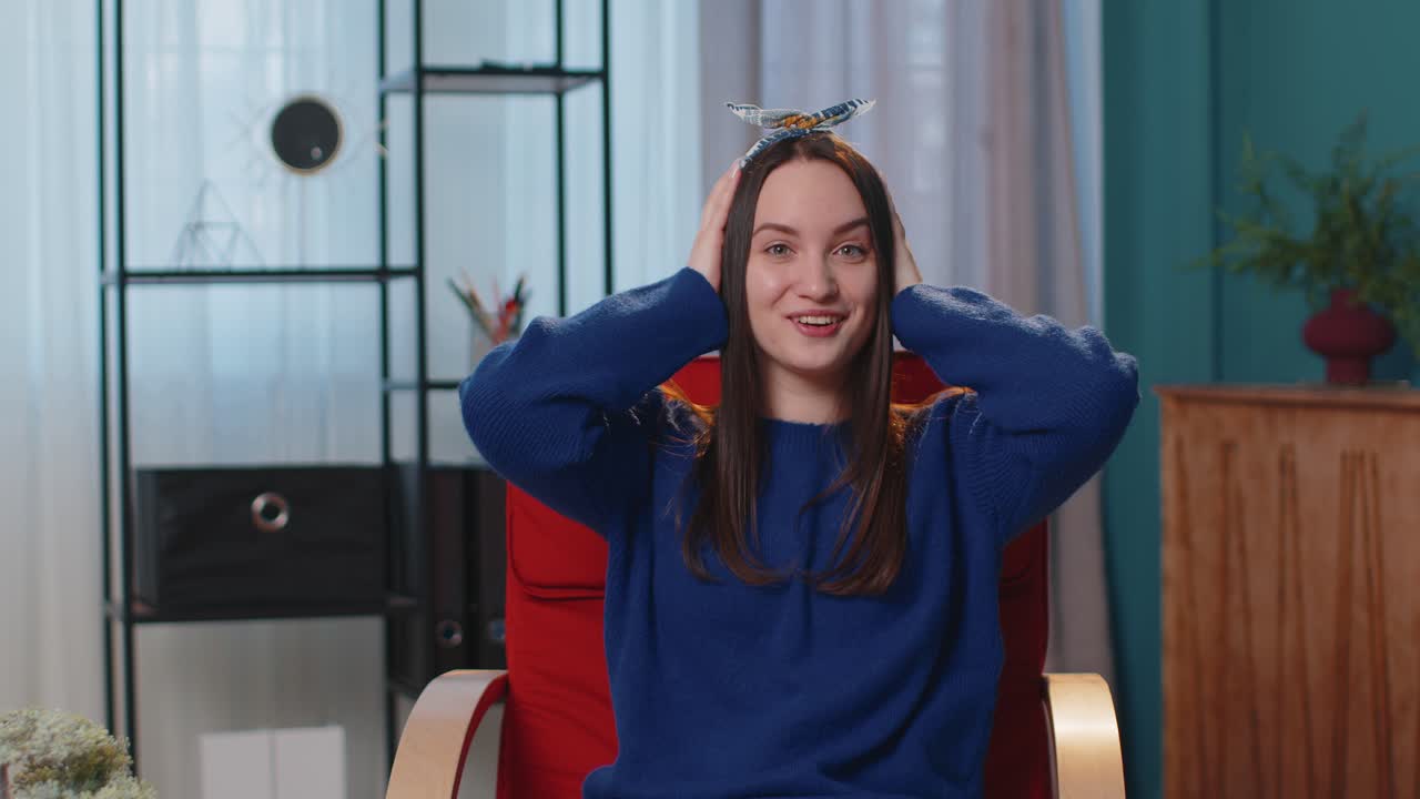 Excited amazed young woman raising hands in surprise shocked by sudden victory at home on chair