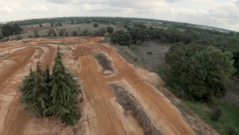 Motocross-rider-on-a-circuit,-red-dirt-terrain-with-trees