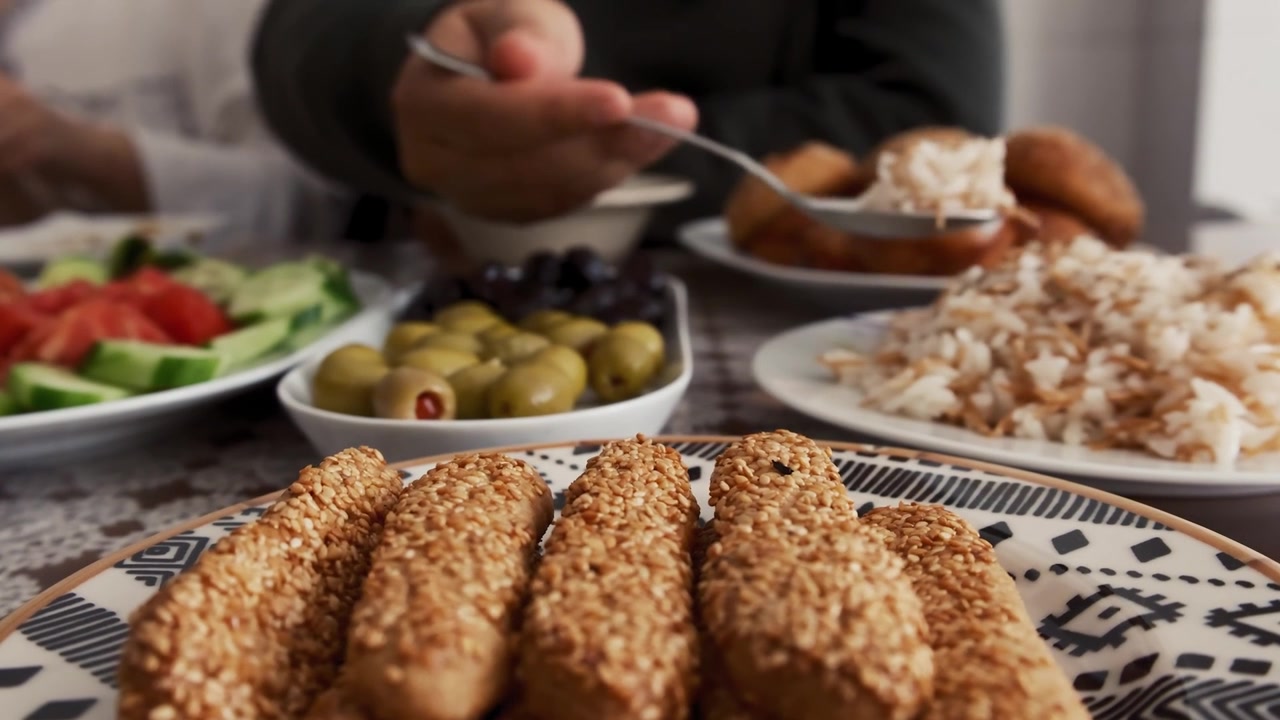 Primo piano di una persona che mangia riso pilaf con un cucchiaio, accanto a biscotti al sesamo, olive e insalata fresca, creando una scena di pasto tradizionale turco con una ricca varietà di piatti.