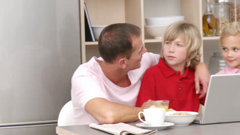 Panorama-of-parents-and-children-having-breakfast-and-using-a-laptop-in-the-kitchen