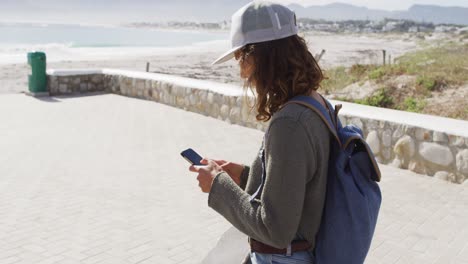 mixed race woman using smartphone on sunny promenade by the sea