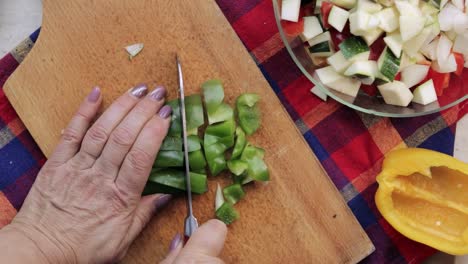 vista de arriba hacia abajo de las manos de la mujer usando un cuchillo santoku y rebanando pimiento dulce verde en una tabla de cortar de madera