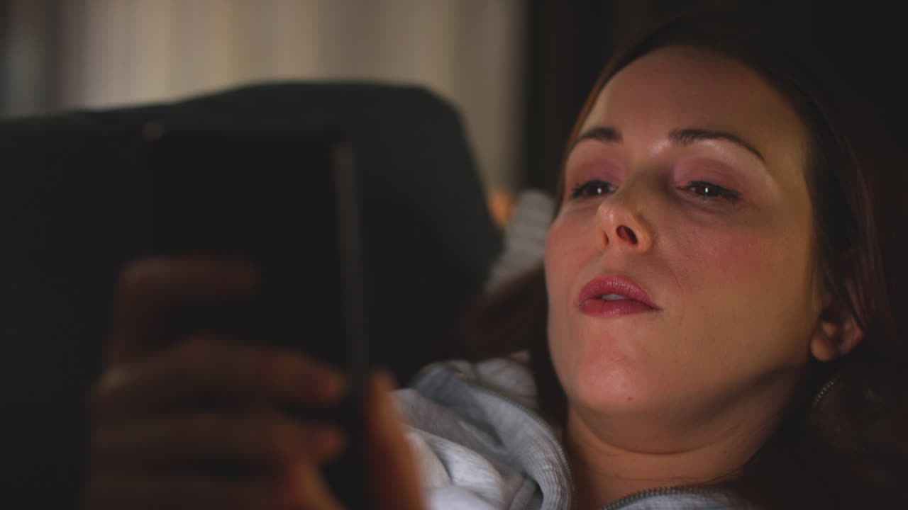 집에서 소파에 누워있는 여성이 스트리밍 또는 영화 또는 쇼를 보거나 휴대 전화로 인터넷을 스크롤합니다.