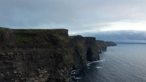 Volar-A-Lo-Largo-De-La-Escarpada-Costa-Rocosa-Del-Mar.-Altas-Paredes-Verticales-Sobre-La-Superficie-Del-Agua-Ondulada-Al-Atardecer.-Acantilados-De-Moher,-Irlanda