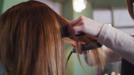 female hairdresser straightening hair of female customer at hair salon