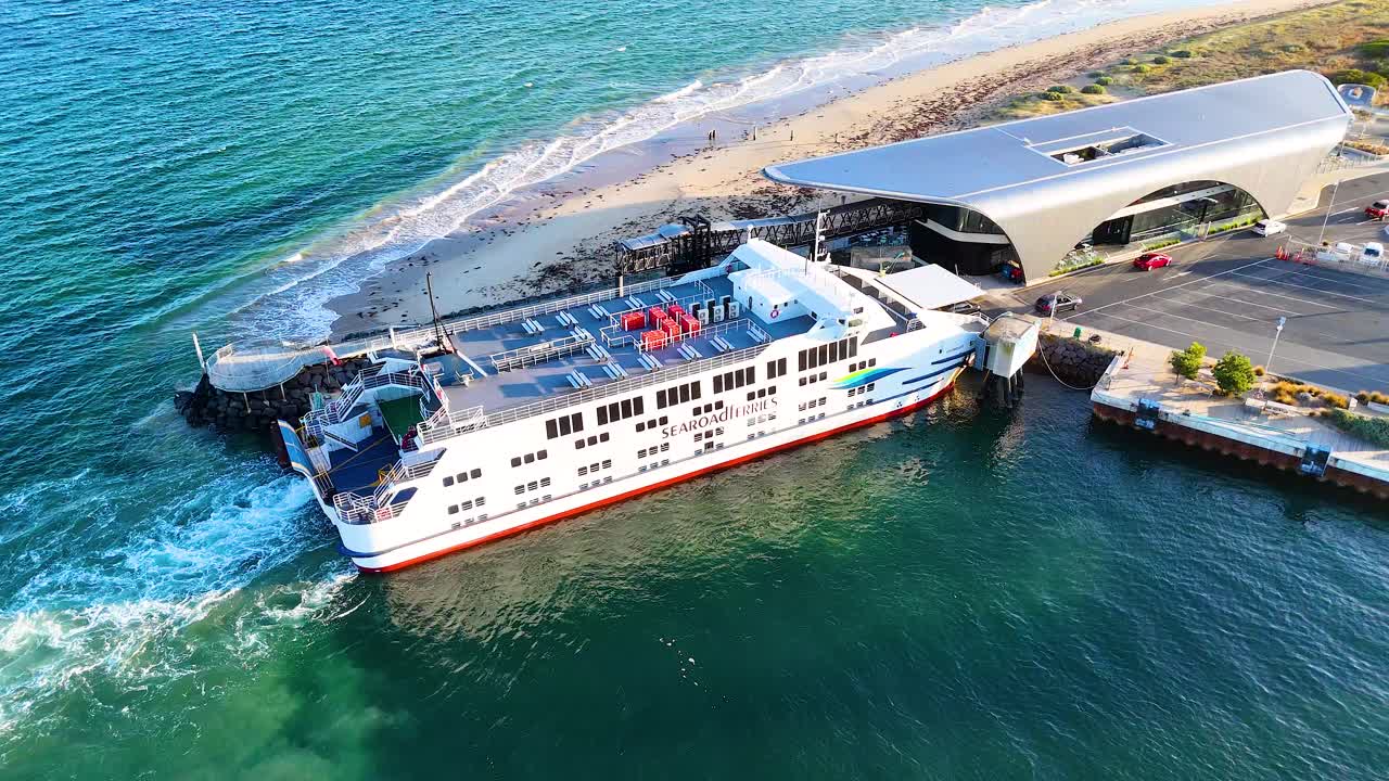 Aerial view of a ferry docking at Queenscliff terminal. Clear skies, vibrant water, and modern architecture create a serene atmosphere