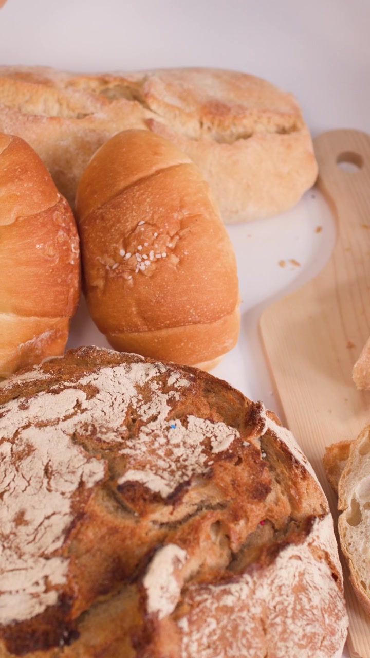 Close-up of hands cutting crusty bread on a wooden board surrounded by various artisan loaves.