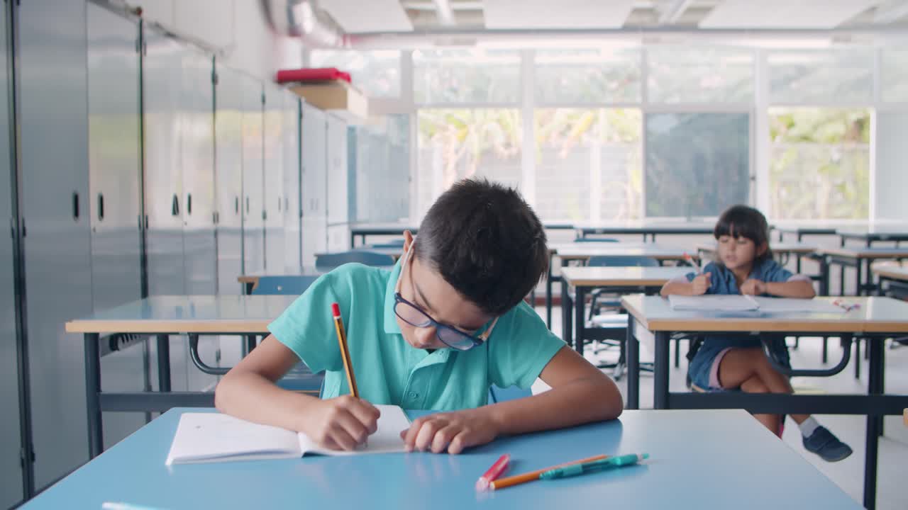 niño alumno latino enfocado con gafas y escribiendo en papel