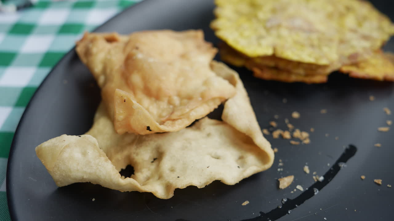 Primo piano di croccanti dolci colombiani ojaldre e tostadas su un piatto scuro. Le texture e i colori risaltano su una tovaglia a quadri. Perfetto per gli appassionati di cibo.