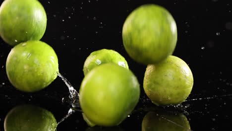 a whole green lemon falls and bounces on a glossy black surface, splashing water under dramatic studio lighting with a high-speed camera setup