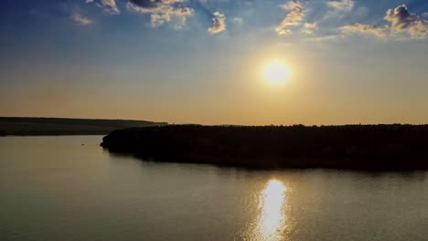 Beautiful evening view on the river at sunset. Golden path in the water from the setting sun on the natural landscape background. Aerial view. Motion camera back.