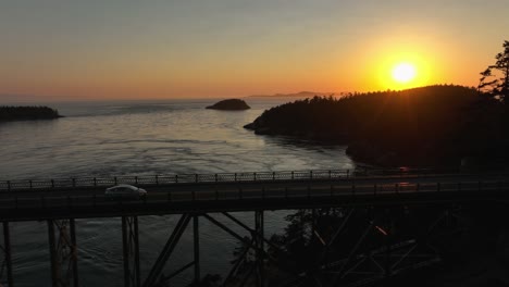 Luftaufnahme,-Die-Eine-Limousine-Verfolgt,-Die-Bei-Sonnenuntergang-über-Die-Deception-Pass-Brücke-Pendelt