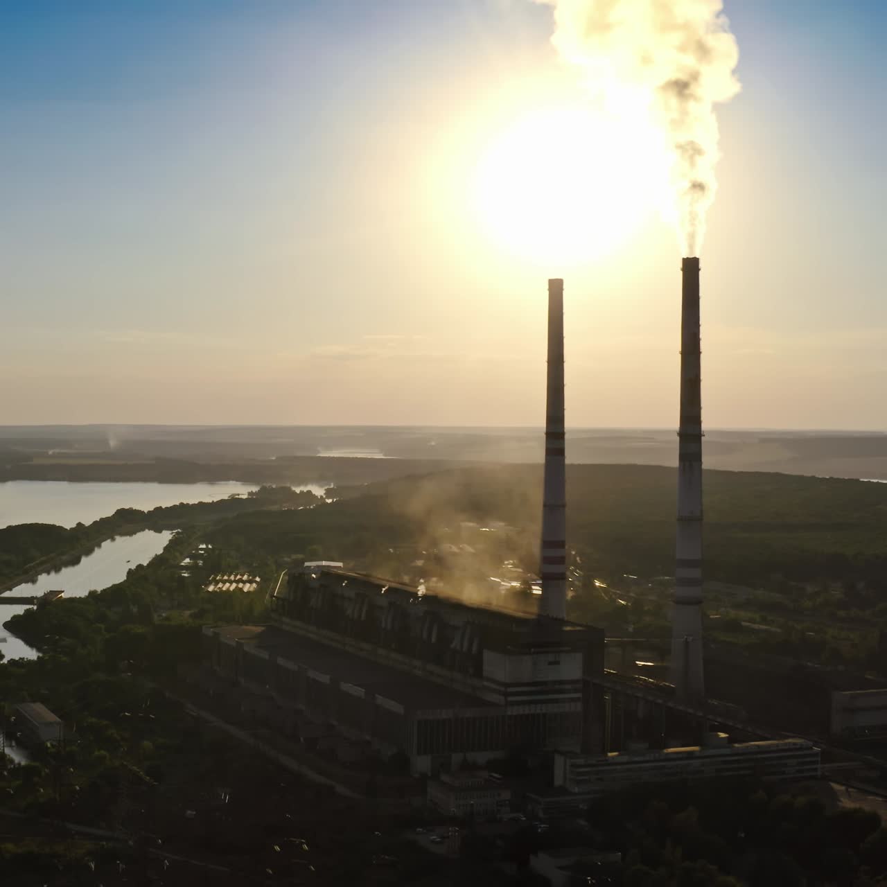 Nature in danger. Harmful factory near the river. Chemical fumes releasing from industrial pipes in the evening. Aerial view.
