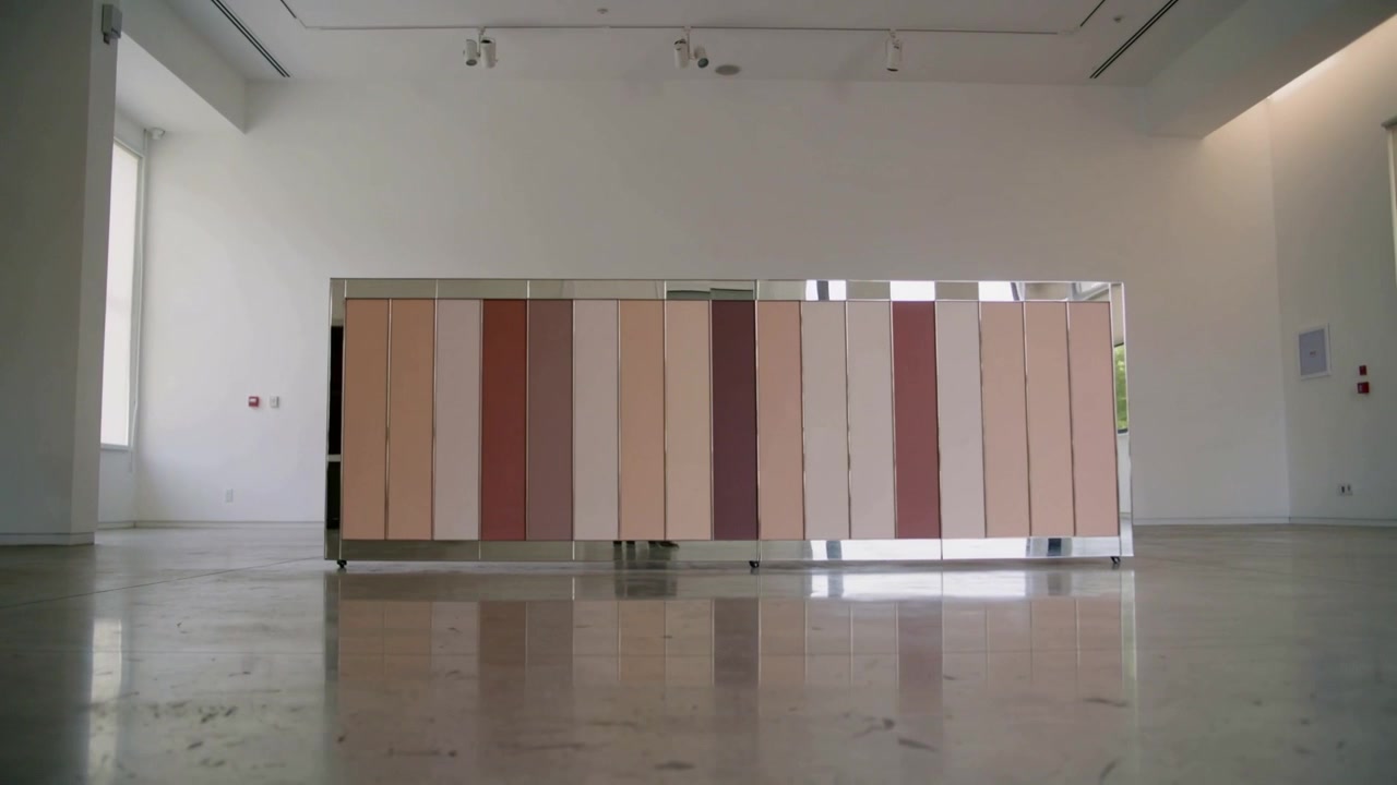 Camera recording stainless-framed cabinet panels shifting in gallery, with reflective floor