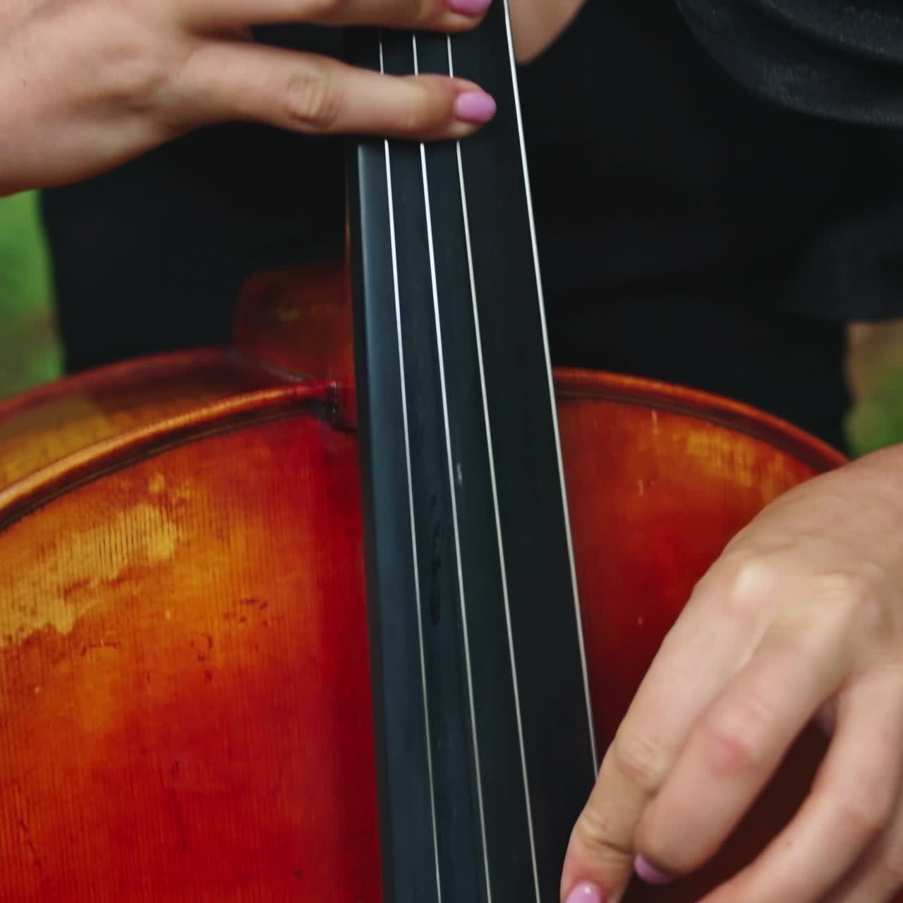 Cello playing. Woman's fingers perform music on strings of a cello. Musical instrument in female's hands outdoors. Close-up.