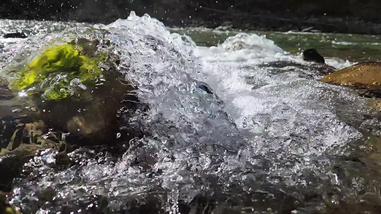 Clear water cascading over rock with algae in slow motion. The background softens into frothy, splashing water as the stream flows away. The mood is cool, refreshing, and energetic