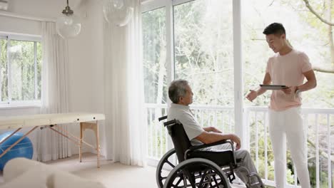 fisioterapeuta masculino diverso con consejos de tabletas y hombre mayor en silla de ruedas, en cámara lenta