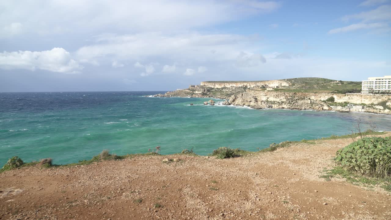 día soleado en la bahía de ghajn tuffieha con olas del mar mediterráneo rodando hacia la orilla