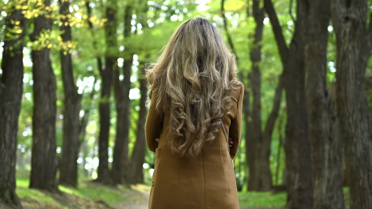 Brunette woman in a coat moving through a park