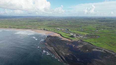 coastline with verdant fields and a sandy beach under a blue sky with clouds at dughmore bay