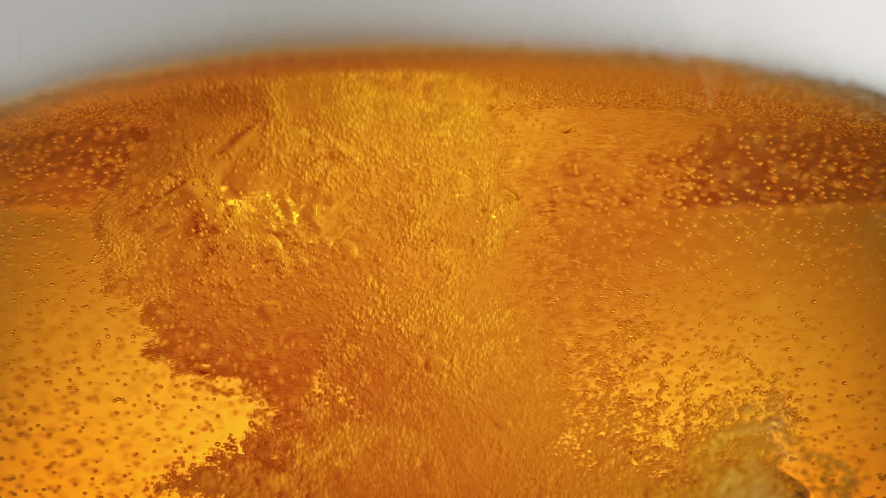 vertido de cerveza desde arriba - flujo turbulento rompe la espuma espumosa liberando nube de burbujas en macro y cámara lenta - vista de bajo ángulo