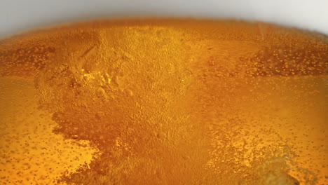 pouring beer from top - turbulent flow breaks frothy foam releasing cloud of bubbles in macro and slow motion - low angle view