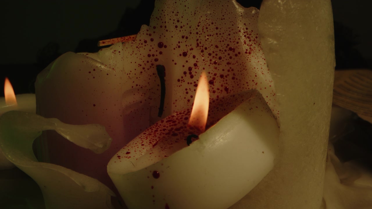 Primo piano inquietante di una candela coperta di sangue con fiamme ardenti. Schizzi di sangue sulle candele.
