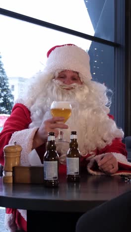 A Santa Claus Figure Relaxes at a Table Enjoying Beer and Cheer a Man Dressed as Santa Claus Sits at a Table Enjoying Beer and Raising a Glass in a Cheerful Toast Adding a Humorous Twist to Holiday Imagery