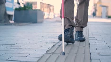 blind person using white cane on straight tactile tiles to navigate road