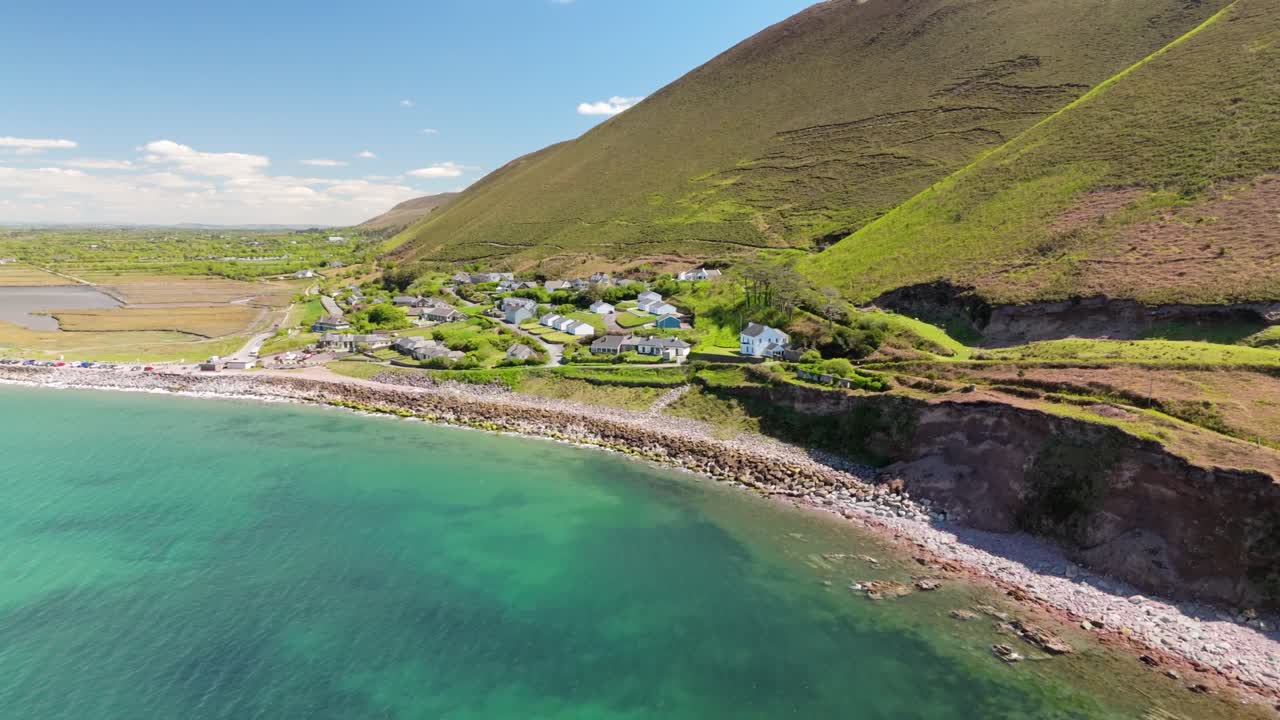 Aerial view of Rosbeigh, Ireland. Flying above beach and green waters of a calm ocean along dramatic coastline, with rolling hills under clear summer skies. Peaceful coastal landscape.