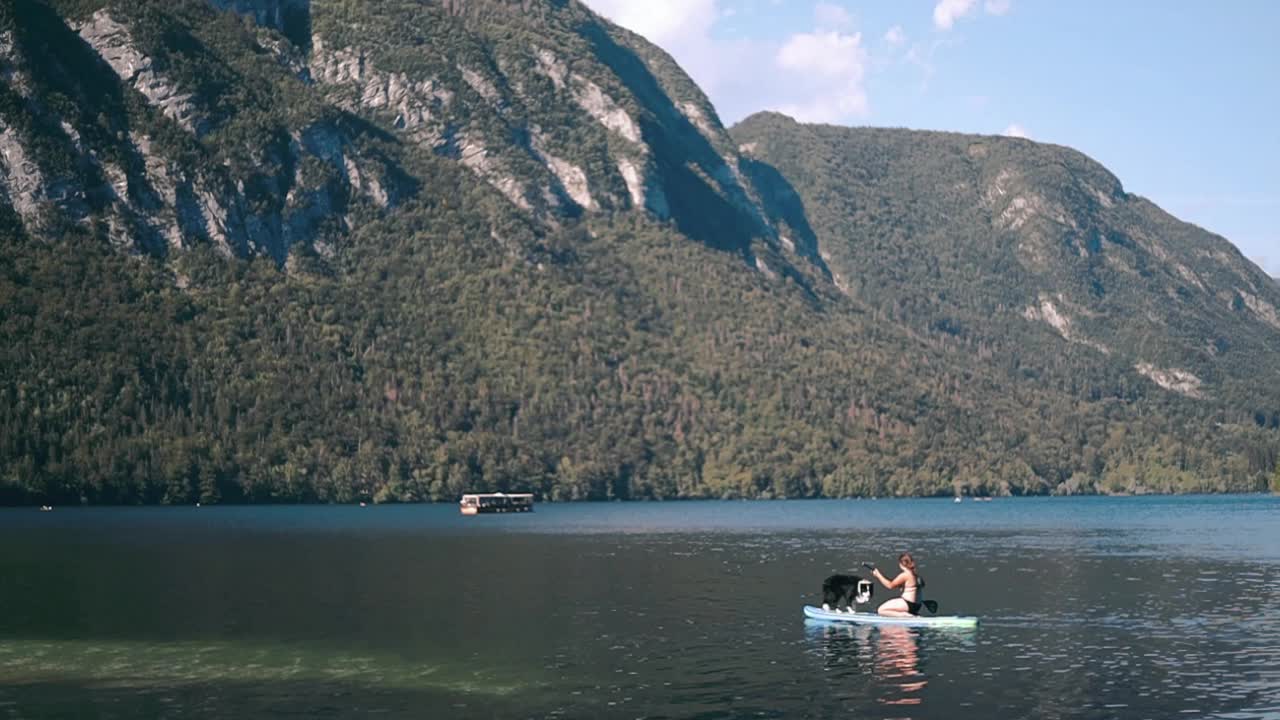 una mujer joven y un perro remando a bordo a través del lago en un sup