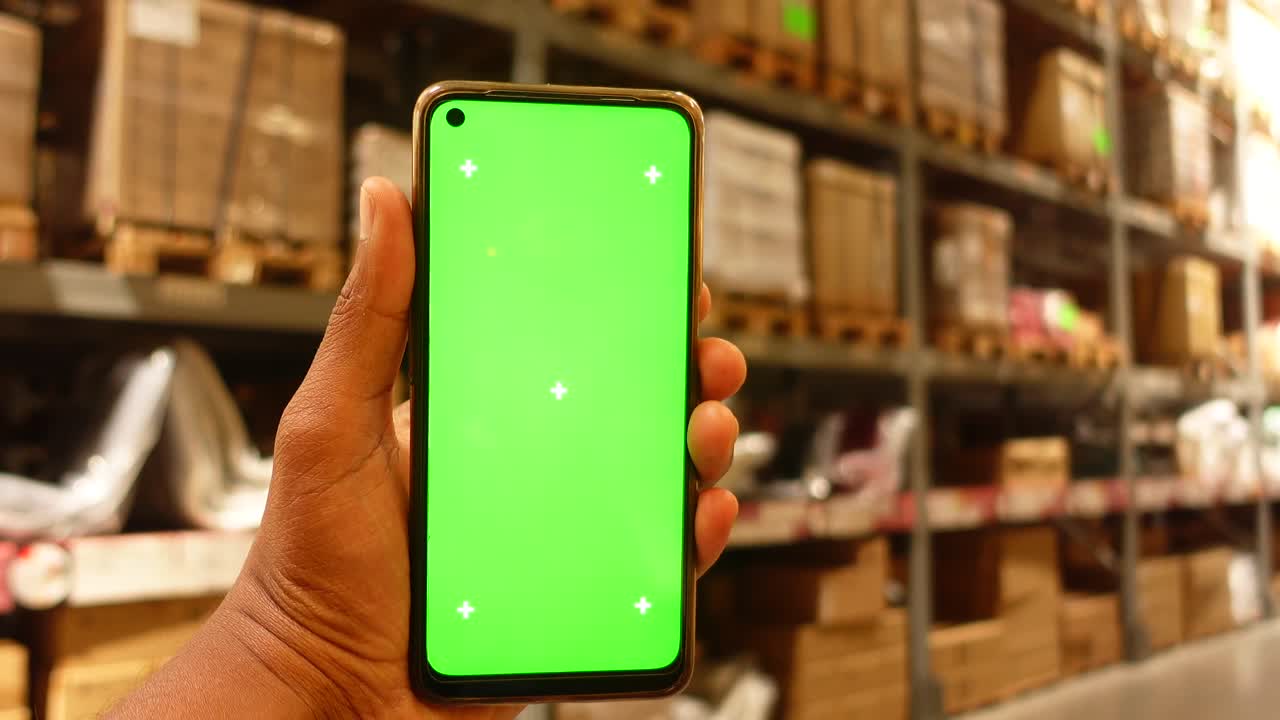 persona con un teléfono inteligente de pantalla verde en un almacén