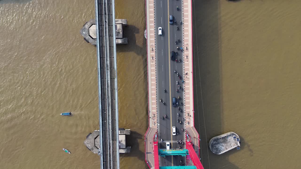 Drone aerial top view of a busy bridge crossing a wide river with cars motorcycles train and boats in
