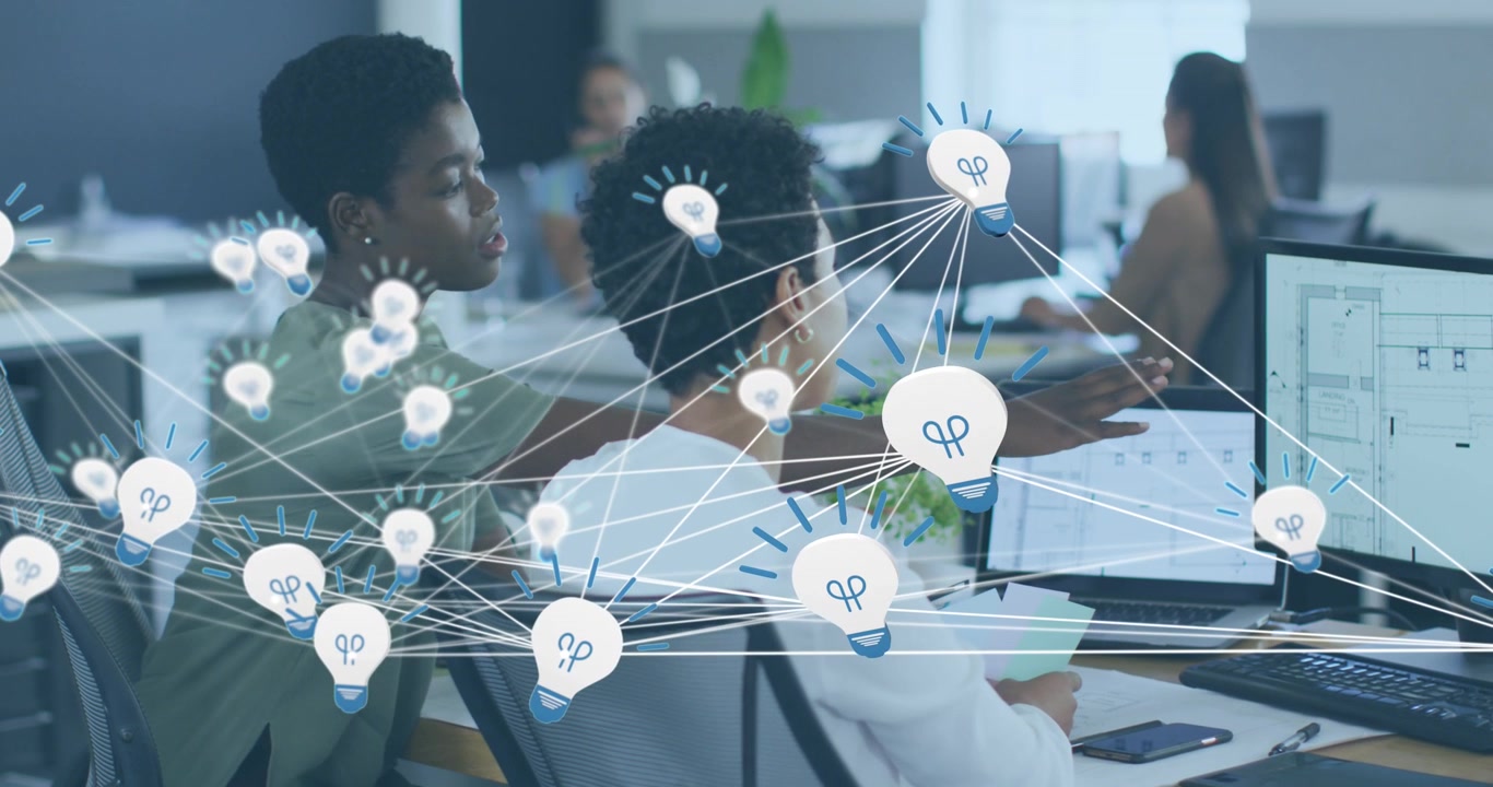 Animation of network of bulb icons over two african american female colleagues discussing at office