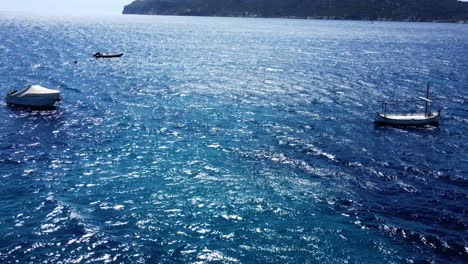 Drone-flight-fast-backwards-over-a-big-ocean-with-island-and-boats-and-waves-on-a-sunny-day-in-Mallorca-Spain